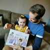 Niña sonriendo mientras su papá lee de un libro personalizado que recibieron por Navidad.
